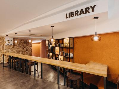 Área moderna de biblioteca con largo mostrador de madera, taburetes y estanterías en ambiente cálido.