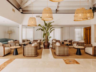 Elegante salón de hotel con lámparas de mimbre, asientos claros y grandes plantas en el centro.