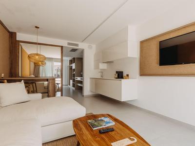 Habitación de hotel moderna con sofá blanco, mesa de madera y TV en la pared en un diseño luminoso y limpio.