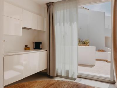 Cocina moderna y luminosa de hotel con suelo de madera marrón y vista a terraza con muebles blancos.