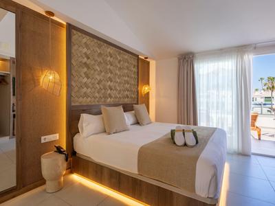 Habitación de hotel moderna con cama grande, iluminación suave y vista a la piscina.