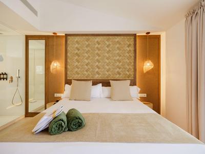 Dormitorio moderno con cama doble, alfombra, toallas y acentos de madera cálidos.