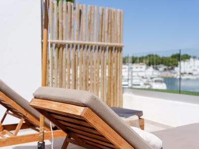 Cómoda tumbona de madera con cojín en una terraza con vista a una marina.