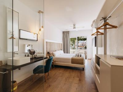 Habitación de hotel moderna con cama doble, escritorio y balcón en tonos neutros.