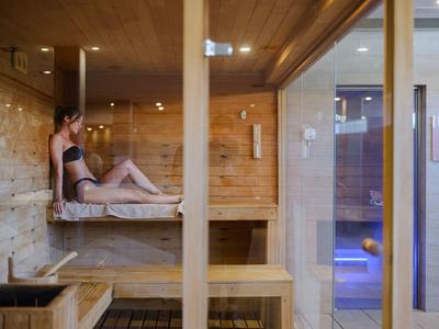 Mujer relajándose en una sauna de madera moderna con puerta de vidrio que da a una zona de piscina.