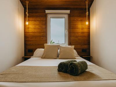 Acogedora habitación de hotel con cama doble, pared de madera y ventana con vista exterior.