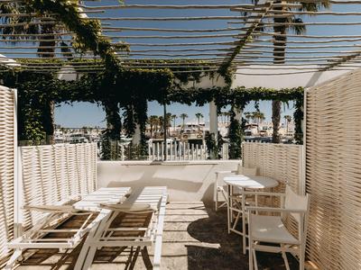 Área de descanso abierta con muebles de madera blanca y una pérgola con plantas al fondo.