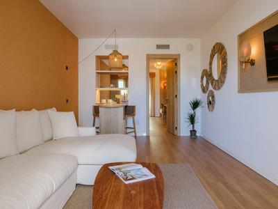 Habitación de hotel moderna con sofá blanco, suelo de madera y cocina abierta.