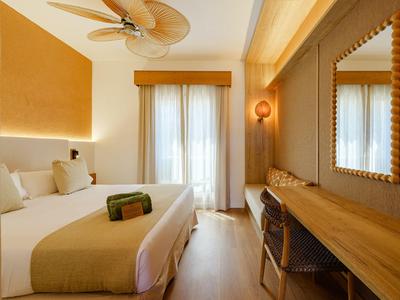 Habitatión de hotel luminosa con cama grande, suelo de madera y ventana con cortinas.