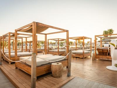 Several wooden canopy sunbeds on a wooden deck at sunset.