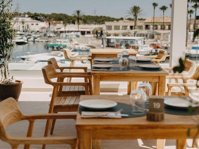 Restaurant terrace with wooden tables overlooking marina and palm trees.