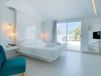 Bright, modern hotel room with double bed, blue armchair, and large glass sliding door to balcony.