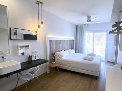 Modern hotel room with double bed, desk, chair, and balcony, bright decor.