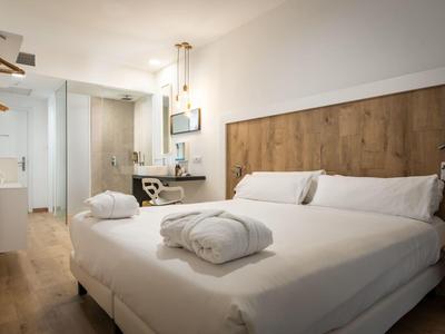 Modern hotel room with bed, wooden headboard, and spacious bathroom.
