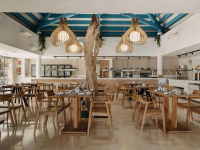 Modern restaurant with wooden furniture, large windows, and natural pendant lights.