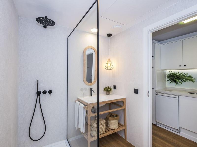 Modern bright bathroom area with walk-in shower, small sink, and adjacent kitchen.