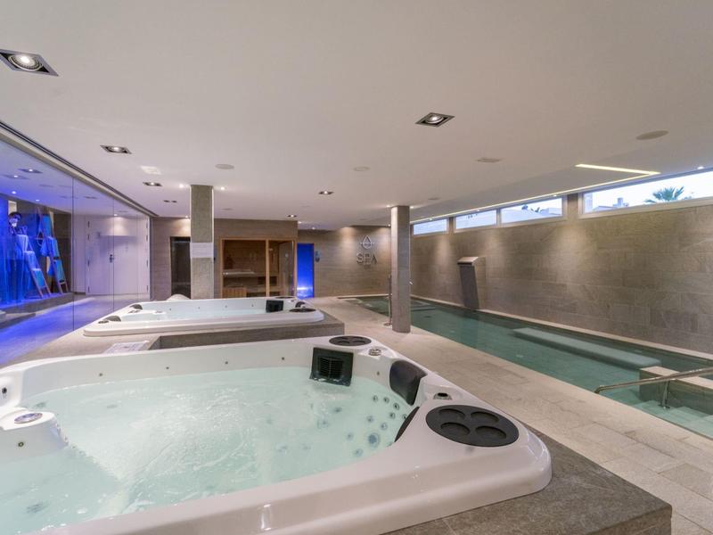 Modern indoor pool area with jacuzzi, long swimming pool, and large windows.