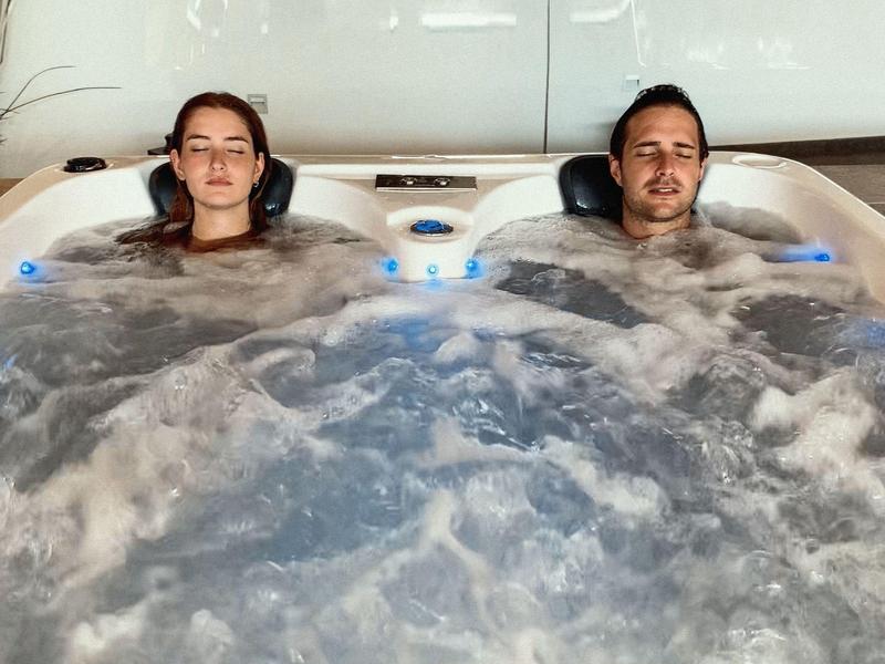 Two people relax in a bubbling hot tub with headrests.