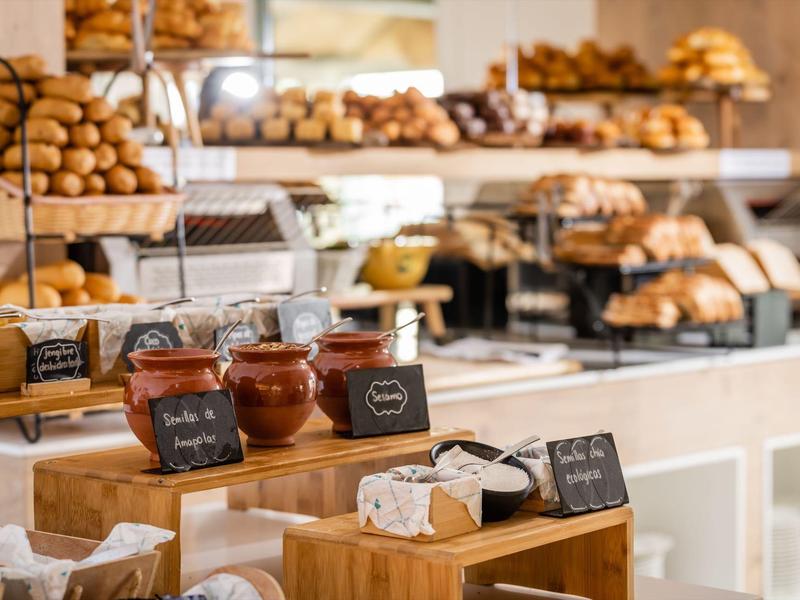 Varied breakfast buffet with jams, rolls, and pastries on wooden furniture.