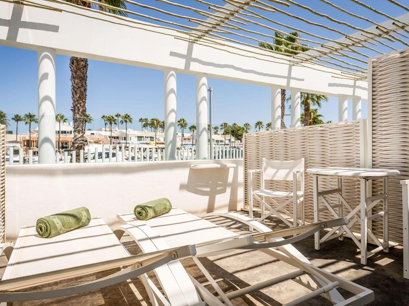 Bright terrace with lounge chairs overlooking palm trees and pool under blue sky.