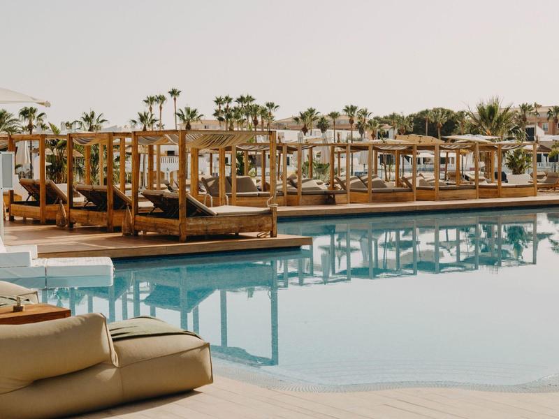 Luxurious pool area with wooden bed seating and palm trees in the background.