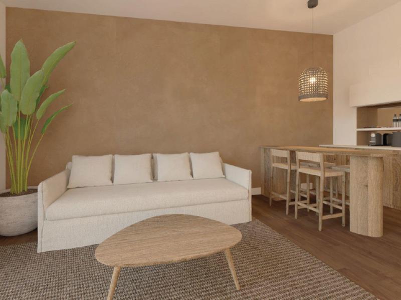 Modern living area with white sofa, wooden table, and kitchenette in warm tones.