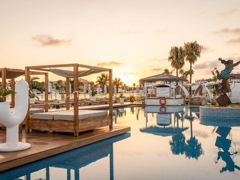 Luxury pool area with canopy beds, sculptures, and sunset at hotel.