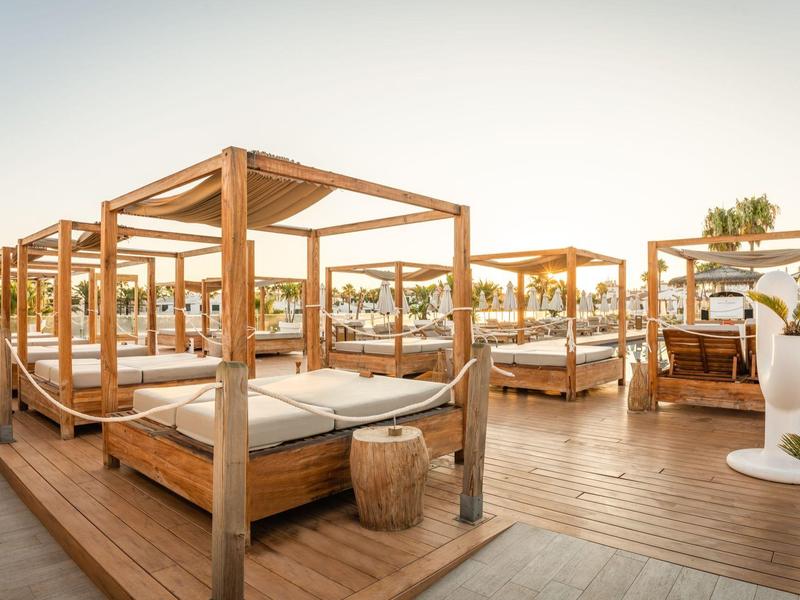 Several wooden canopy sunbeds on a wooden deck at sunset.