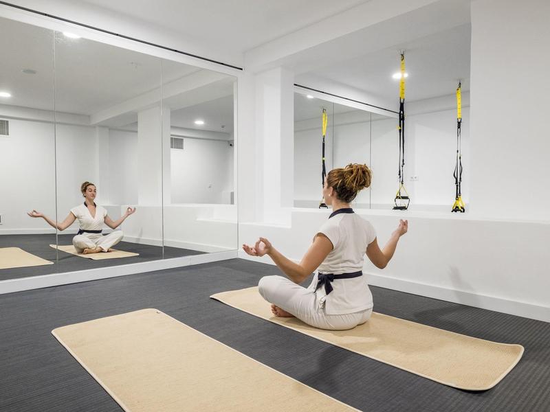 Woman practicing meditation in a white room on a yoga mat with mirrored wall.