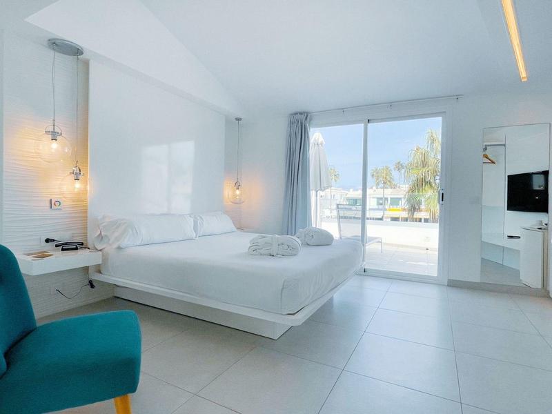 Bright, modern hotel room with double bed, blue armchair, and large glass sliding door to balcony.