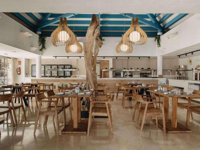 Modern restaurant with wooden furniture, large windows, and natural pendant lights.