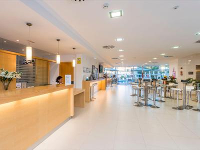 Jasna i nowoczesna lobby hotelowa z recepcją, miejscami do siedzenia i dużymi oknami wpuszczającymi światło dzienne.