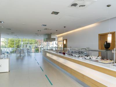 Nowoczesna kuchnia hotelowa z bufetem, jasnym wnętrzem, dużymi oknami i nakrytymi stołami.