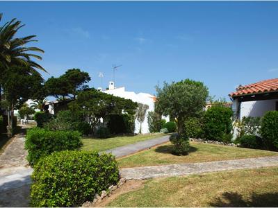 Garten mit Rasen, Palmen, Sträuchern und weißen Häusern unter blauem Himmel.