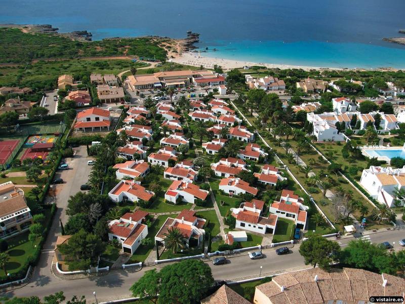 Luftaufnahme eines Wohngebiets mit weißen Häusern und roten Dächern nahe einem blauen Meer.