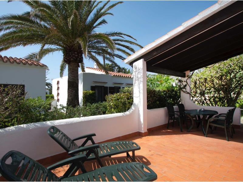 Terrasse mit orangem Boden, Palmen, Liegestühlen und Sitzbereich unter überdachtem Bereich.