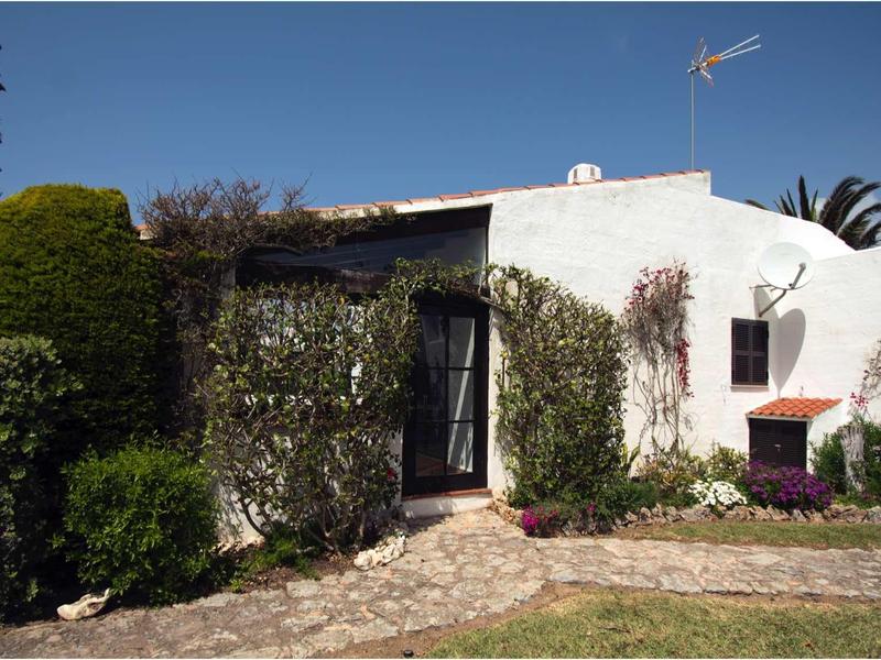 Weißes Haus mit flachem Dach, grünen Sträuchern und Steinweg im Vorgarten.