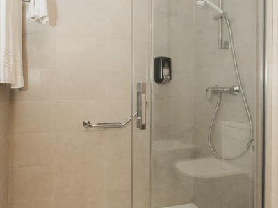 Modern shower enclosure with glass sliding doors and handheld shower in a bright bathroom.