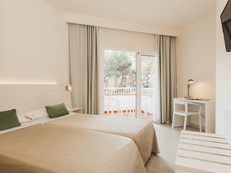 Bright hotel room with two single beds, balcony access, and modern desk