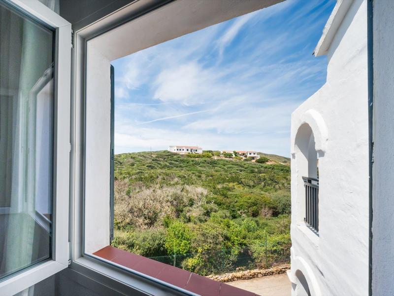 Open raam met uitzicht op groene heuvels en blauwe lucht met wolken.
