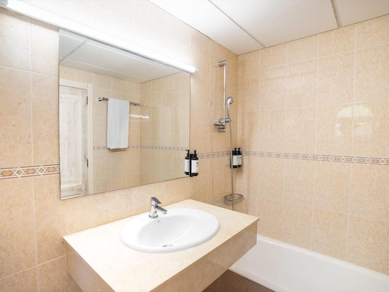 Heldere badkamer met wastafel, grote spiegel, badkuip en beige betegelde muren.