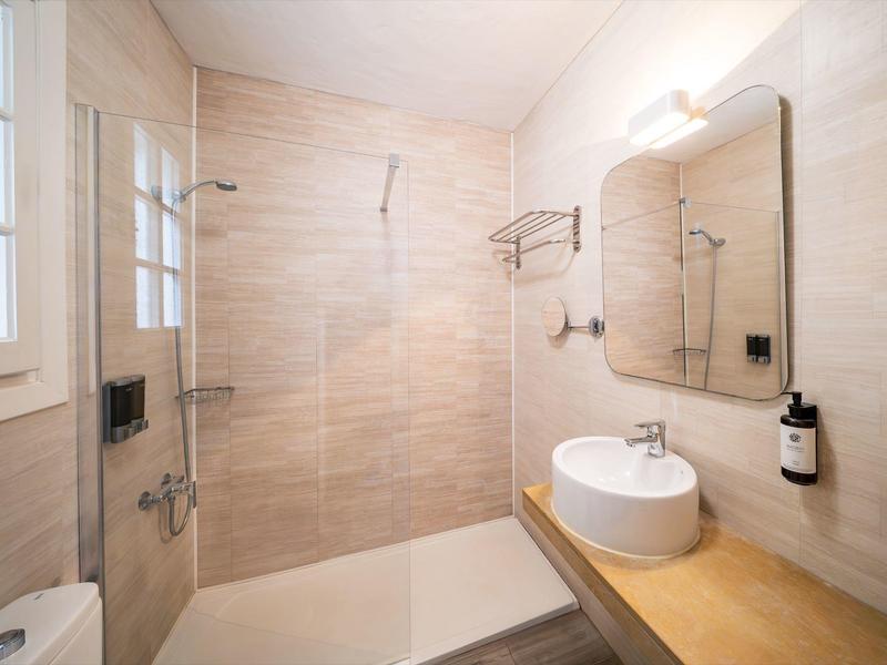 Moderne badkamer met inloopdouche, grote spiegel, ronde wastafel en beige betegelde muren.