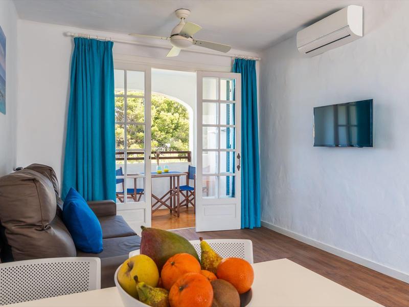 Knusse hotelkamer met een bank, fruitschaal, blauwe gordijnen en balkon met tafel en stoelen.