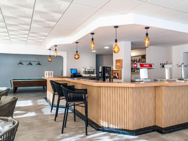 Modern hotelbar met houten balie, zwarte krukken en hanglampen in een ruime kamer.