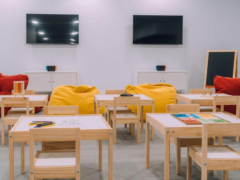 Lichte kamer met kleine houten tafels, gele zitzakken en rode banken voor ontspanning.