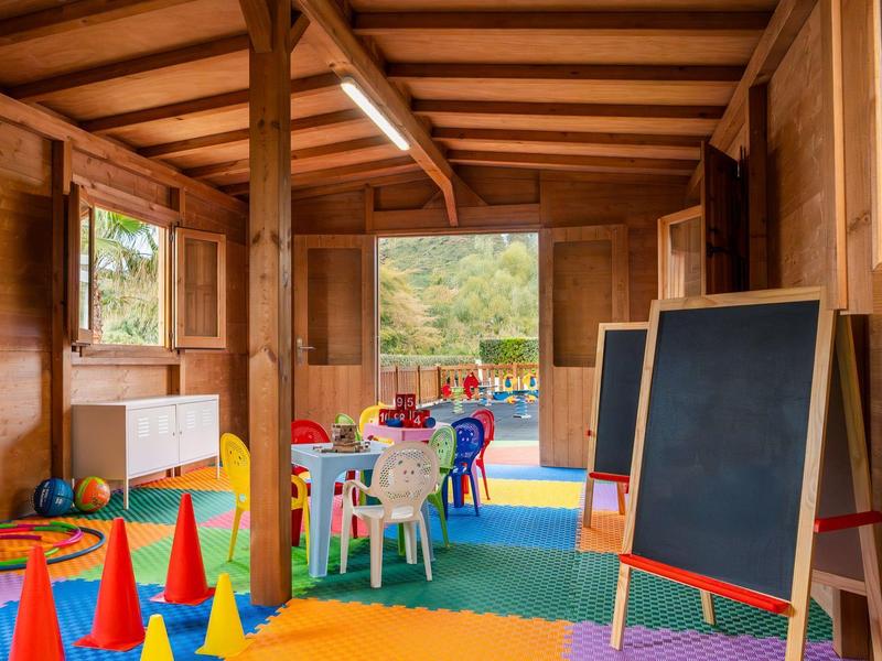 Heldere, kleurrijke kinderkamer met tafels, stoelen, kegels en schoolbord, uitzicht op raam.