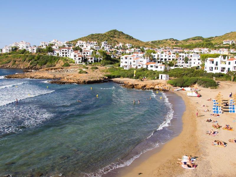 Zonnig strand met parasols, liggende mensen en witte huizen op de heuvel bij de zee.
