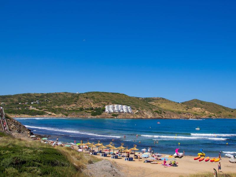 Strand met zonaanbidders, parasols en heuvels op de achtergrond op een zonnige dag.