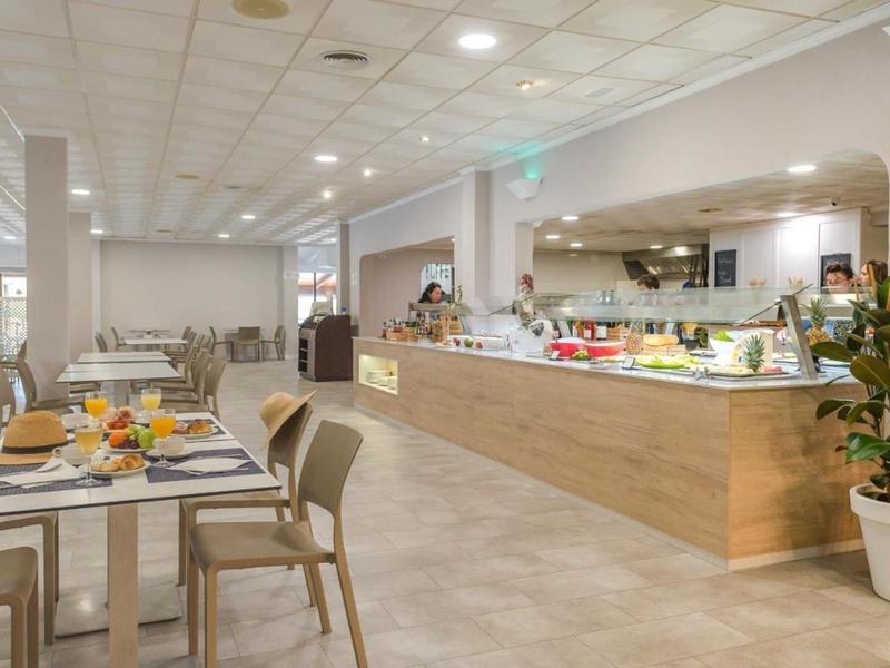 Lichte hotelbuffetruimte met houten balies, zitplaatsen en planten onder inbouwspots.