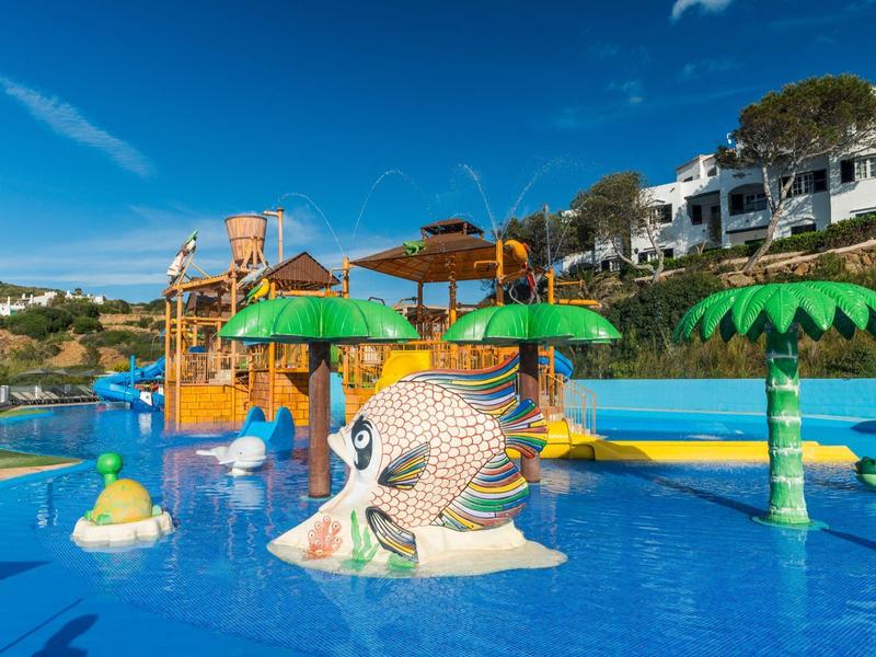 Kleurrijk waterpark met glijbanen, fonteinen en parasols in een heldere resortomgeving.
